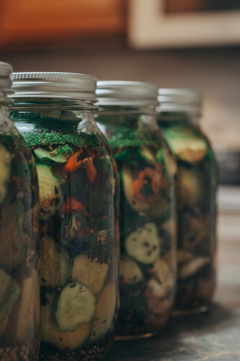 Bocaux de courgettes et de légumes variés en saumure, éclairés par une lumière chaude