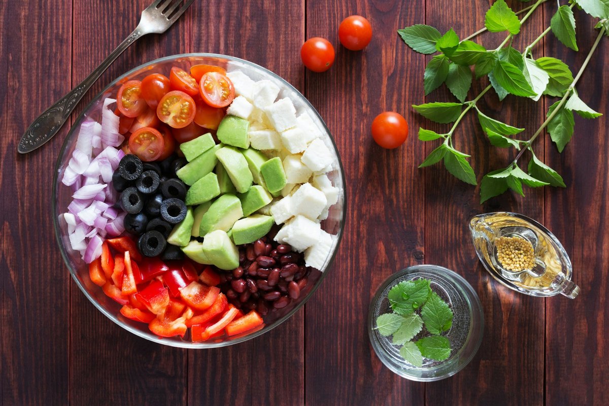 Bol de crudités colorées : tomates cerises, avocat, olives, haricots rouges, poivron et oignon