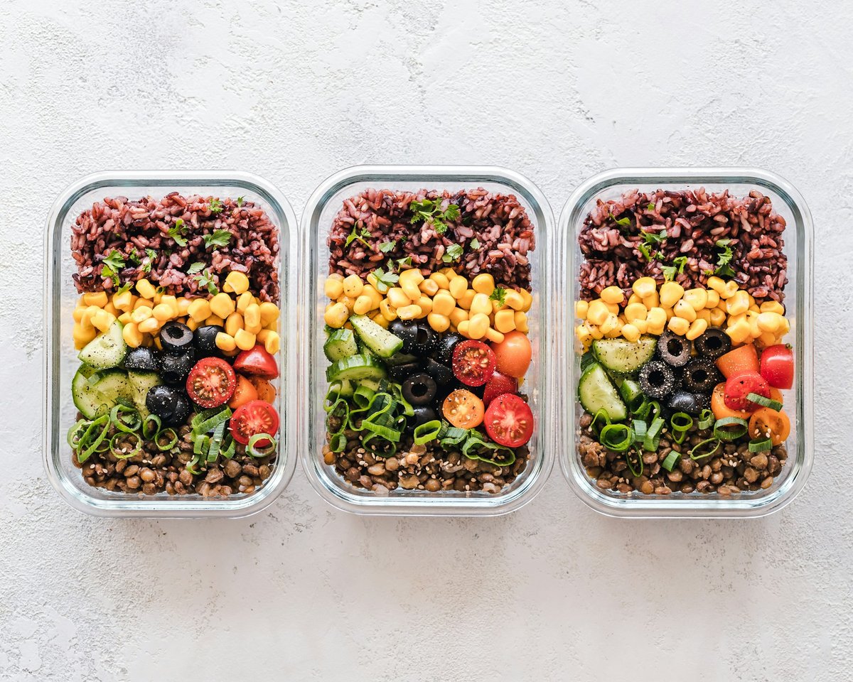 Trois boîtes repas en verre garnies de riz noir, maïs, olives, tomates et lentilles