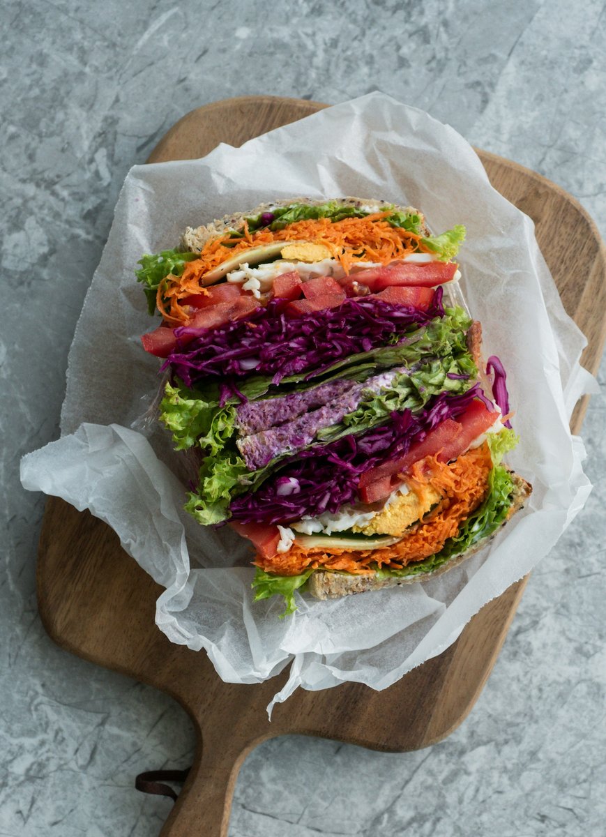 Sandwich garni de chou rouge, carottes râpées, tomate et salade, emballé dans du papier