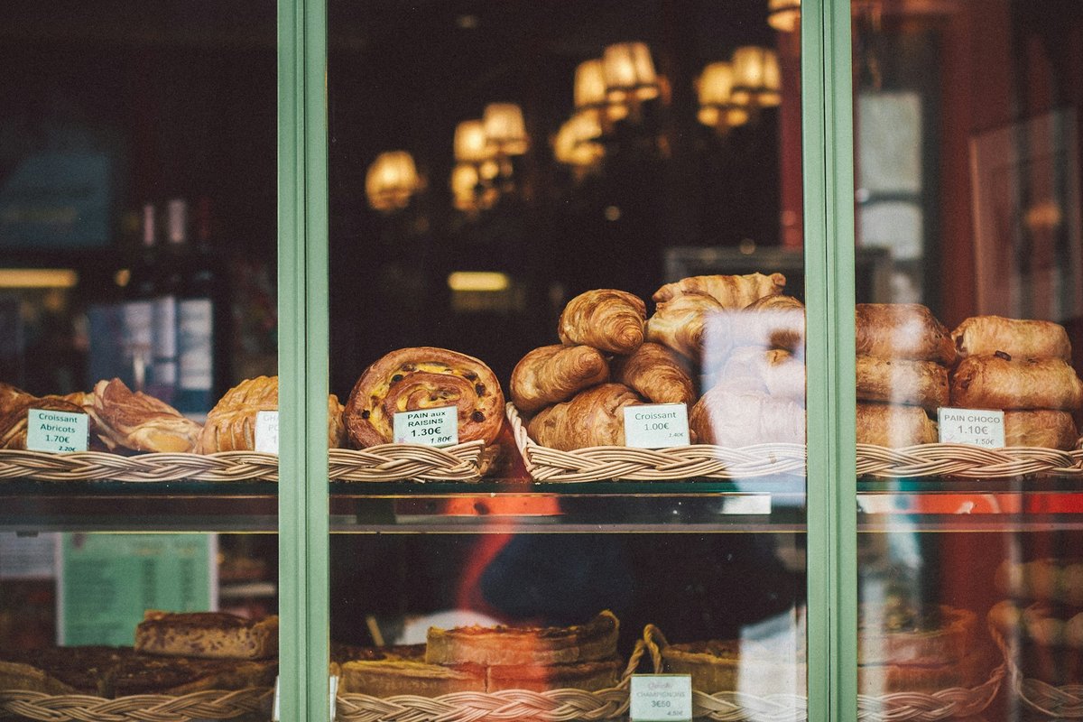 Vitrine de boulangerie aux montants peints en vert, viennoiseries disposées dans des corbeilles
